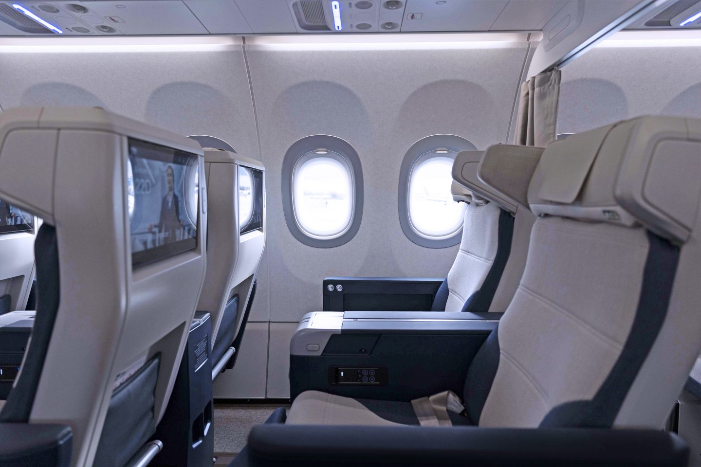 Eine Reihe von Premium Economy-Sitzplätzen mit eingeschalteten Bildschirmen in den Kopfstützen und sichtbaren Sitzverstellungsknöpfen. 