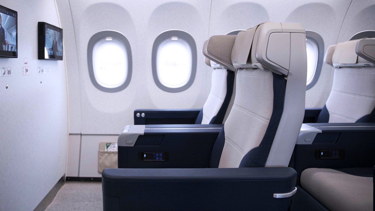 Primera fila de asientos de Premium Economy con espacio adicional para las piernas y pantallas instaladas en la pared.
