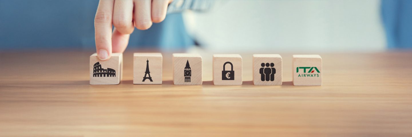 A hand picking up a block from a row of wooden blocks with travel icons and the ITA Airways logo.