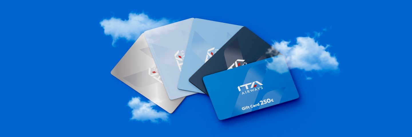 Quattro Gift Card di ITA Airways disposte su uno sfondo blu con nuvole.