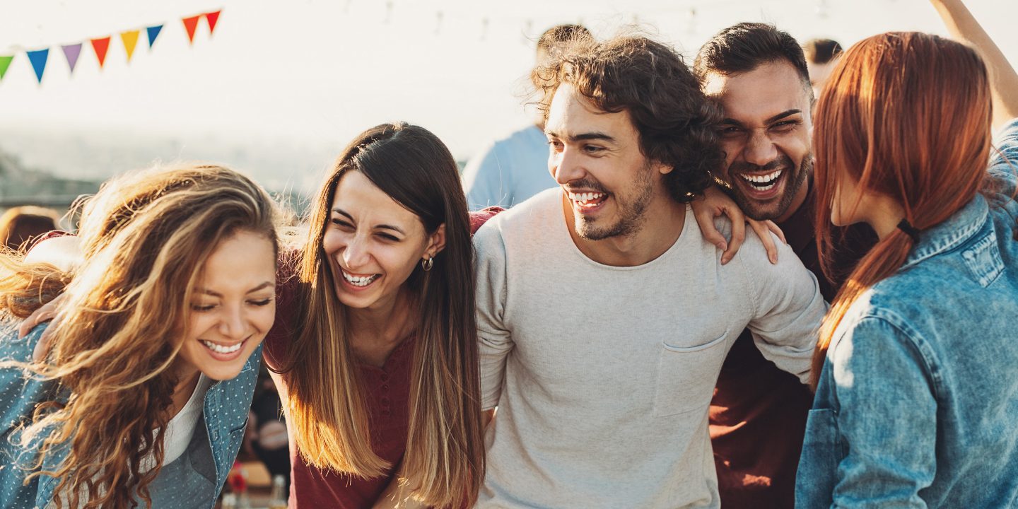 A group of friends laughing and hugging at an outdoor party.