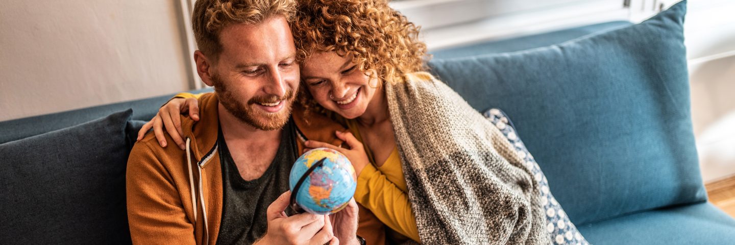 Two people sitting on a sofa hold a small globe in their hands.