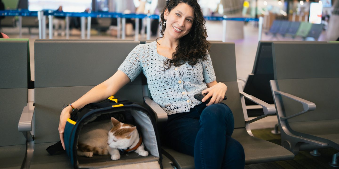 Un passager assis dans un aéroport à côté d’une cage de transport dans laquelle se trouve un chat.