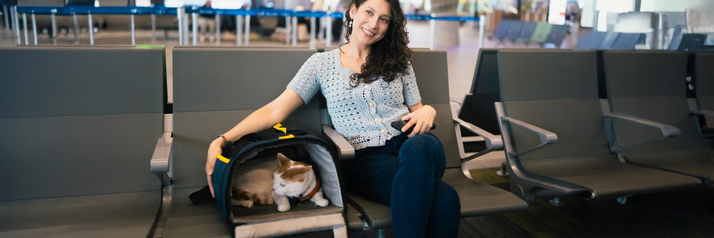 Un passager assis dans un aéroport à côté d’une cage de transport dans laquelle se trouve un chat.