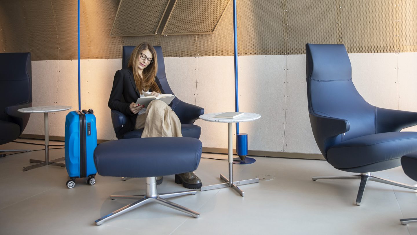 Un passager assis dans l’espace de relaxation du salon Runway avec une valise.