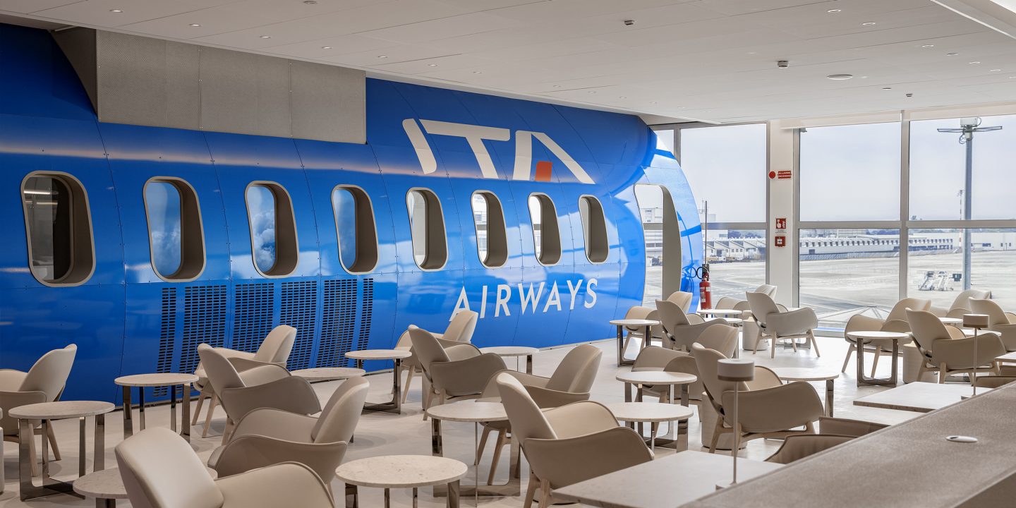 Interior of the Runway Lounge in Milan Linate with an ITA Airways fuselage-shaped wall.