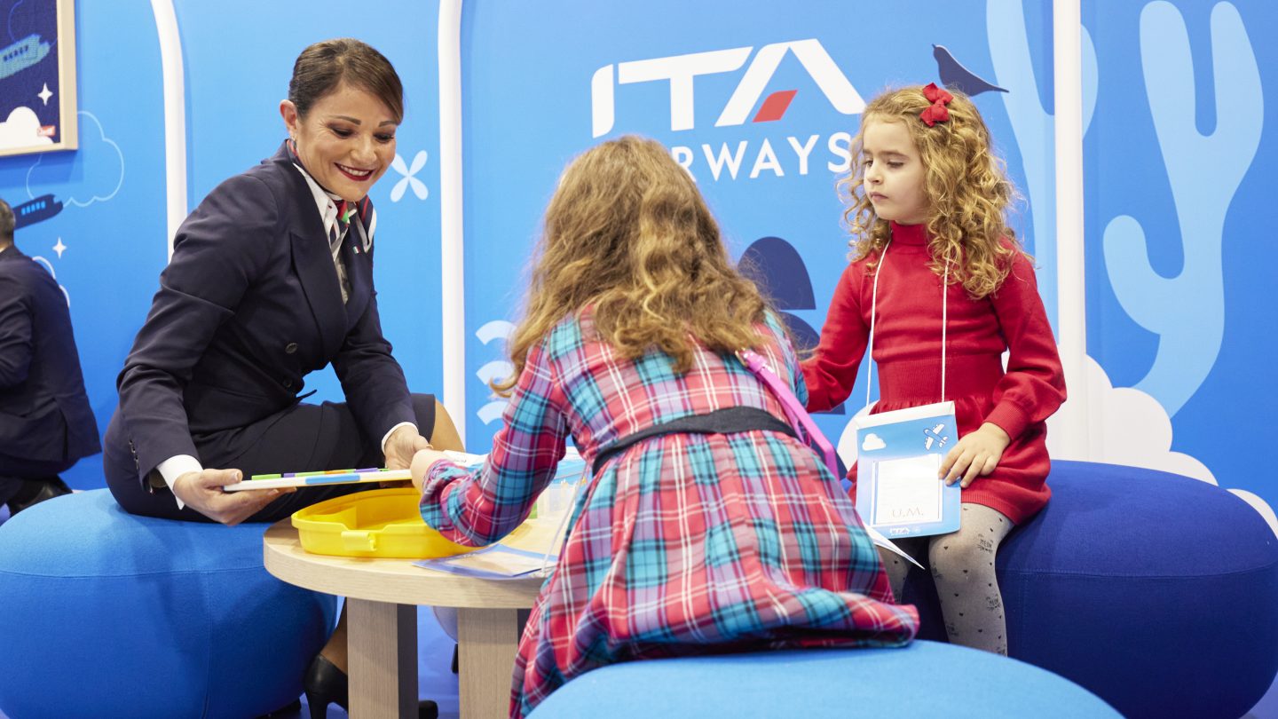 Un membre du personnel d’ITA Airways s’occupe de deux enfants dans une zone d’aéroport dédiée.