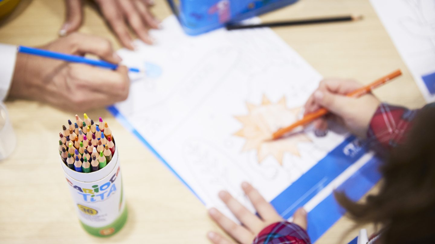 Des mains coloriant un dessin sur une table avec des crayons de couleur.