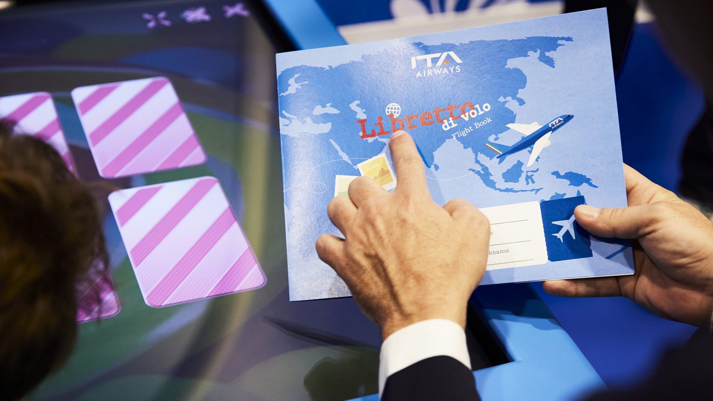 Un adulte tenant un livret pour enfants d’ITA Airways.