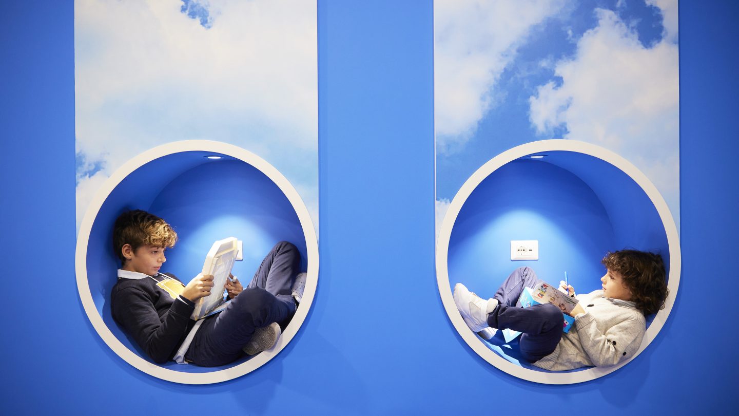 Deux enfants assis dans des niches murales circulaires recouvertes d’un papier peint avec des motifs de nuages.