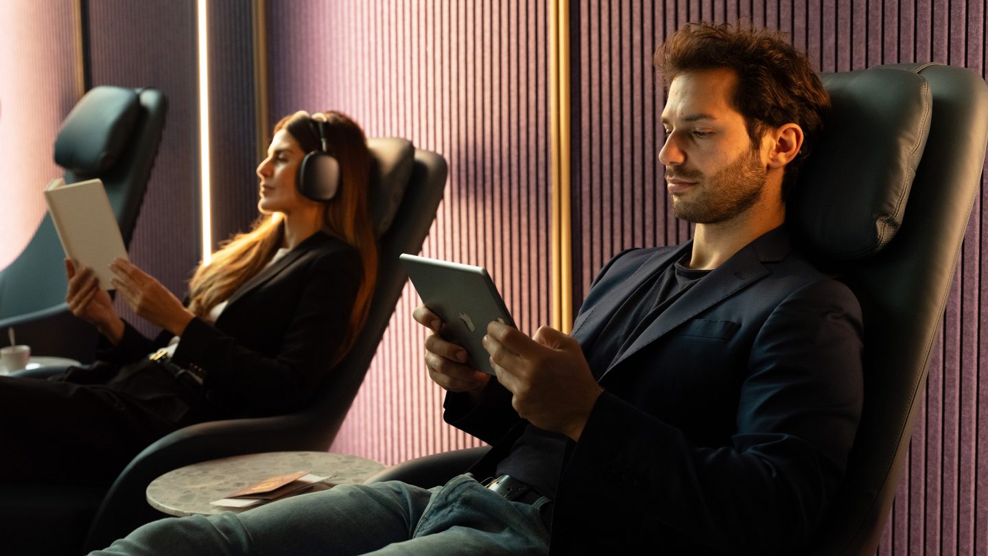 Two passengers seated in armchairs, one with a tablet and the other with a book.