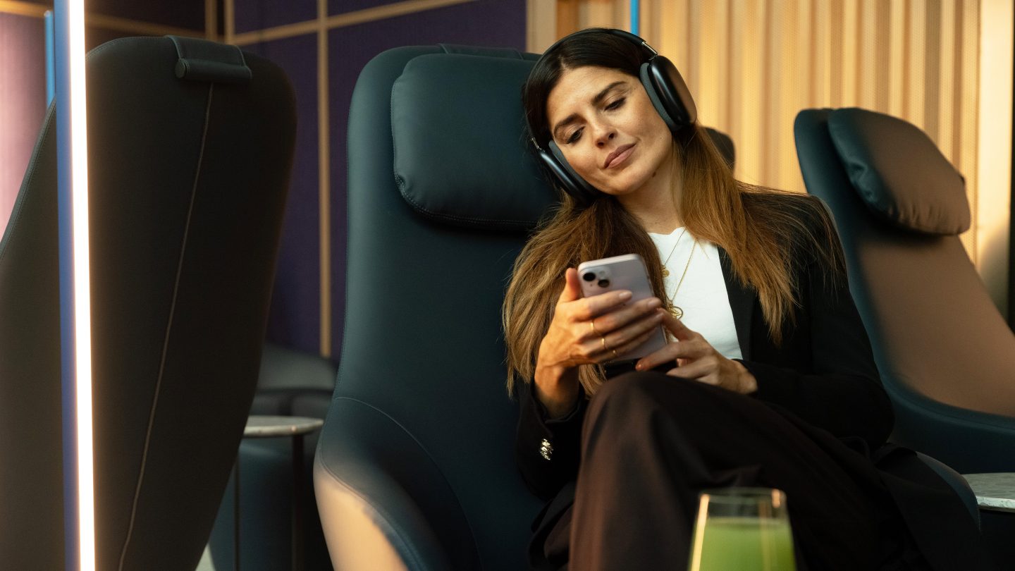 A passenger seated in an armchair looking at her smartphone with headphones on.