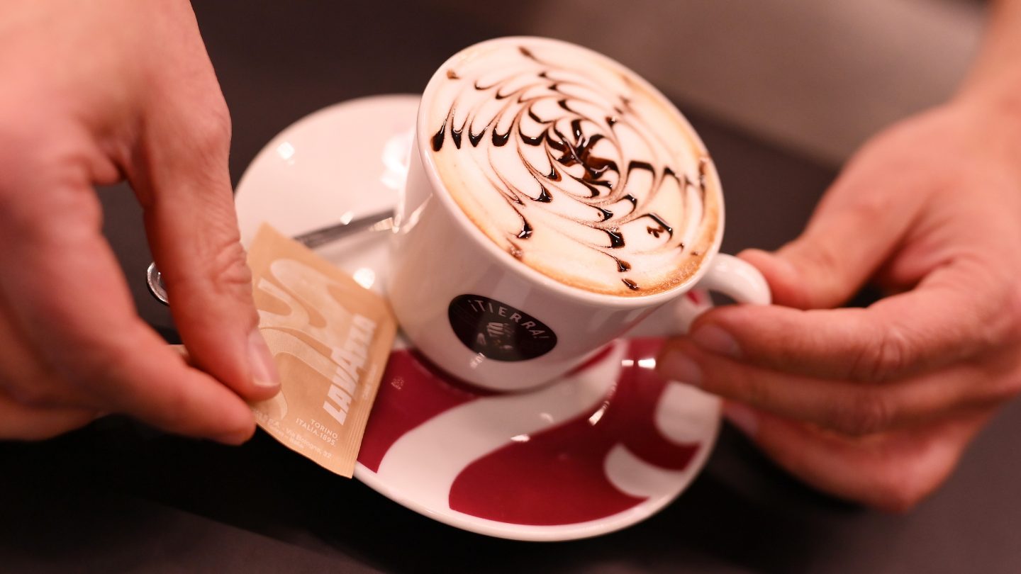 A cappuccino cup on a saucer with a sugar packet.
