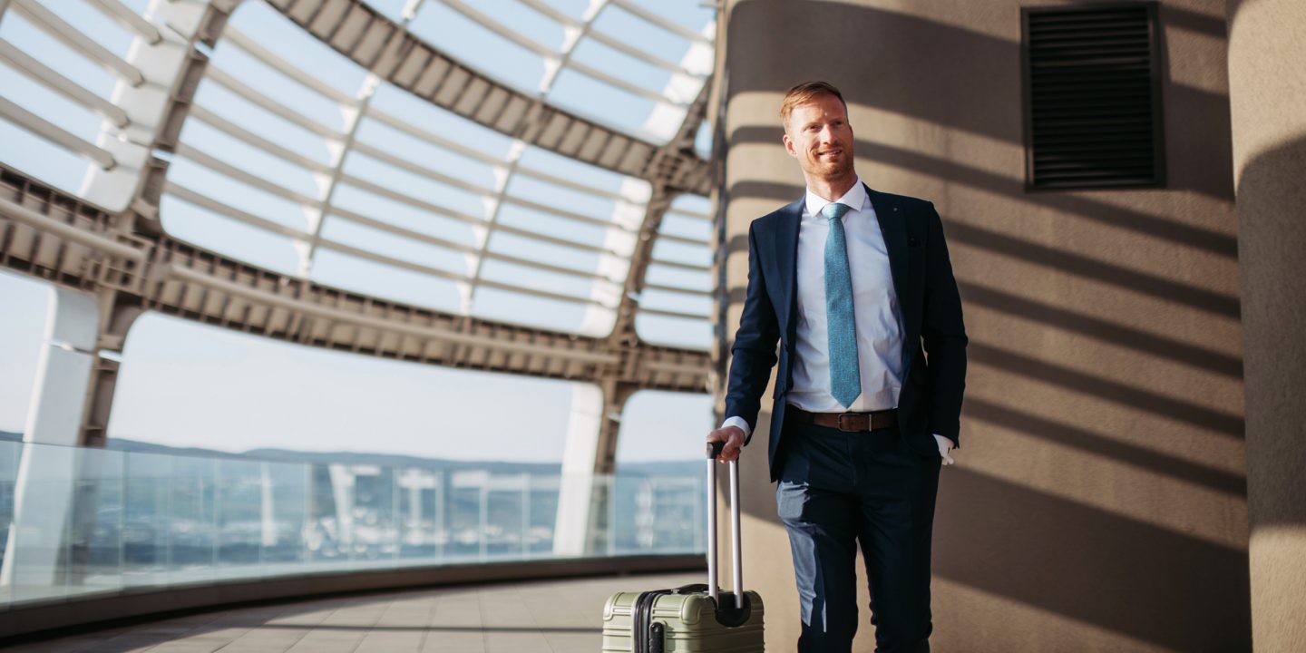 A man in a suit and tie stands holding a suitcase, ready for travel or a business meeting.