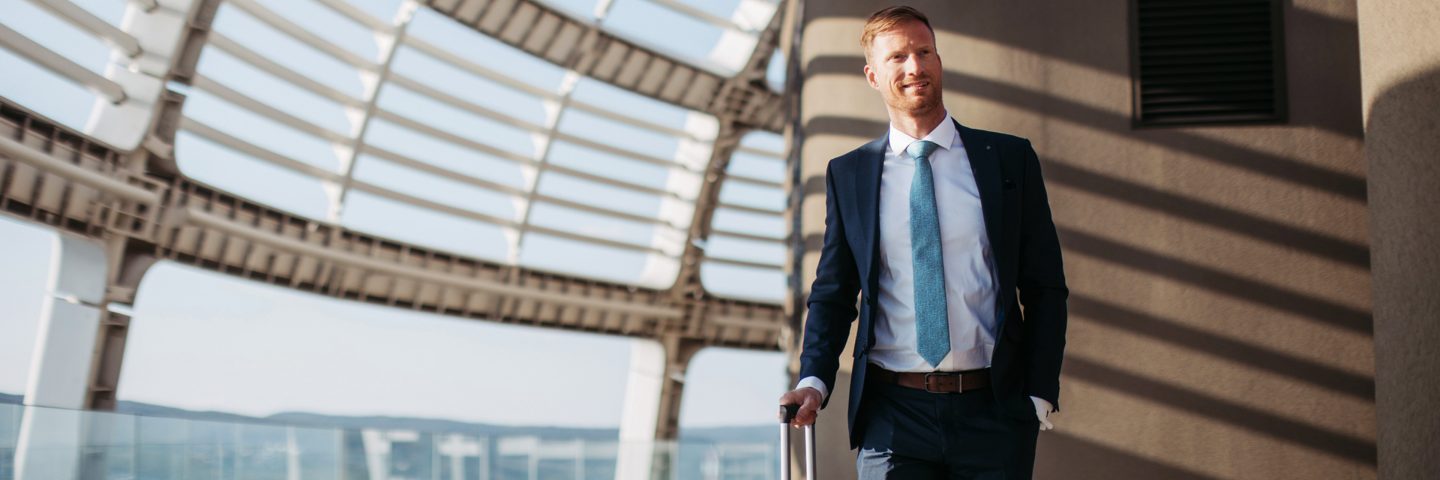 A man in a suit and tie stands holding a suitcase, ready for travel or a business meeting.