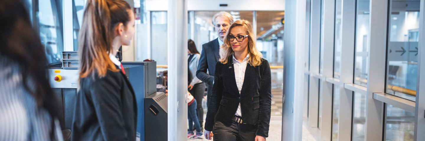 A woman in a business suit walks through an airport terminal, carrying a briefcase and looking focused.