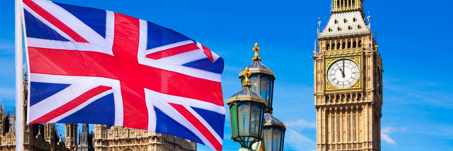 A United Kingdom flag flying with the Big Ben in the background.