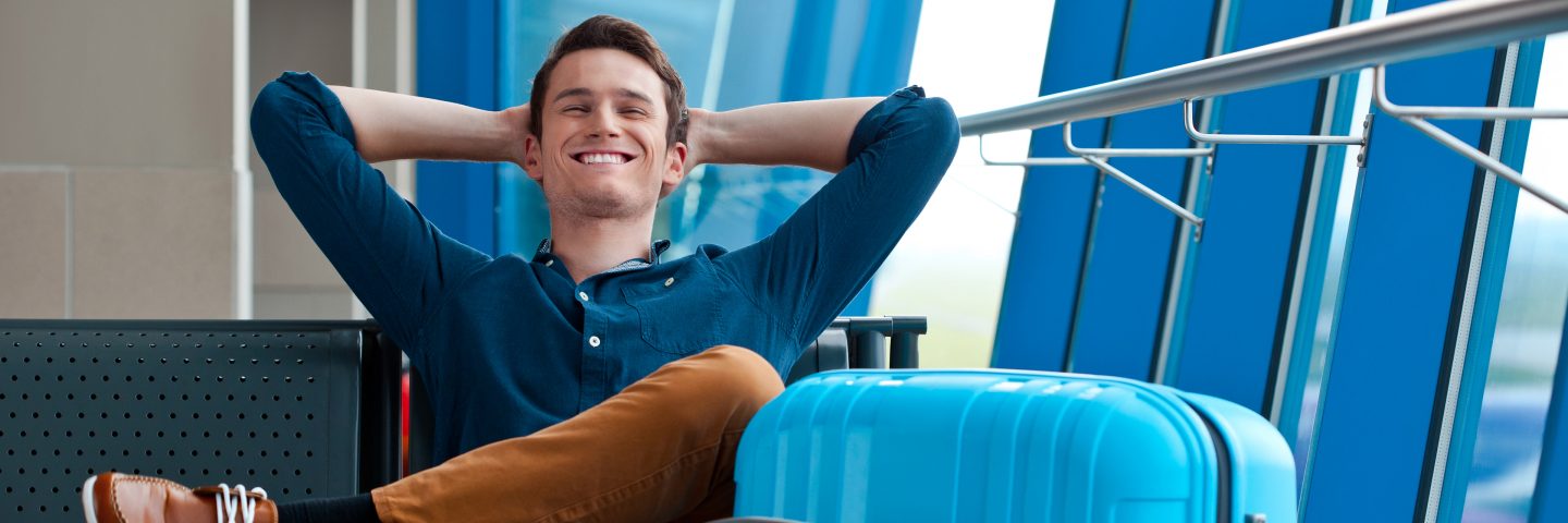 A man seated at the airport with suitcases beside him.