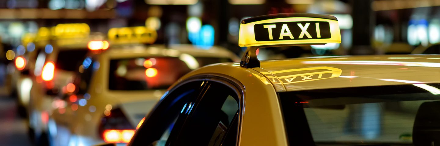Taxis with illuminated roof signs lined up on a street.