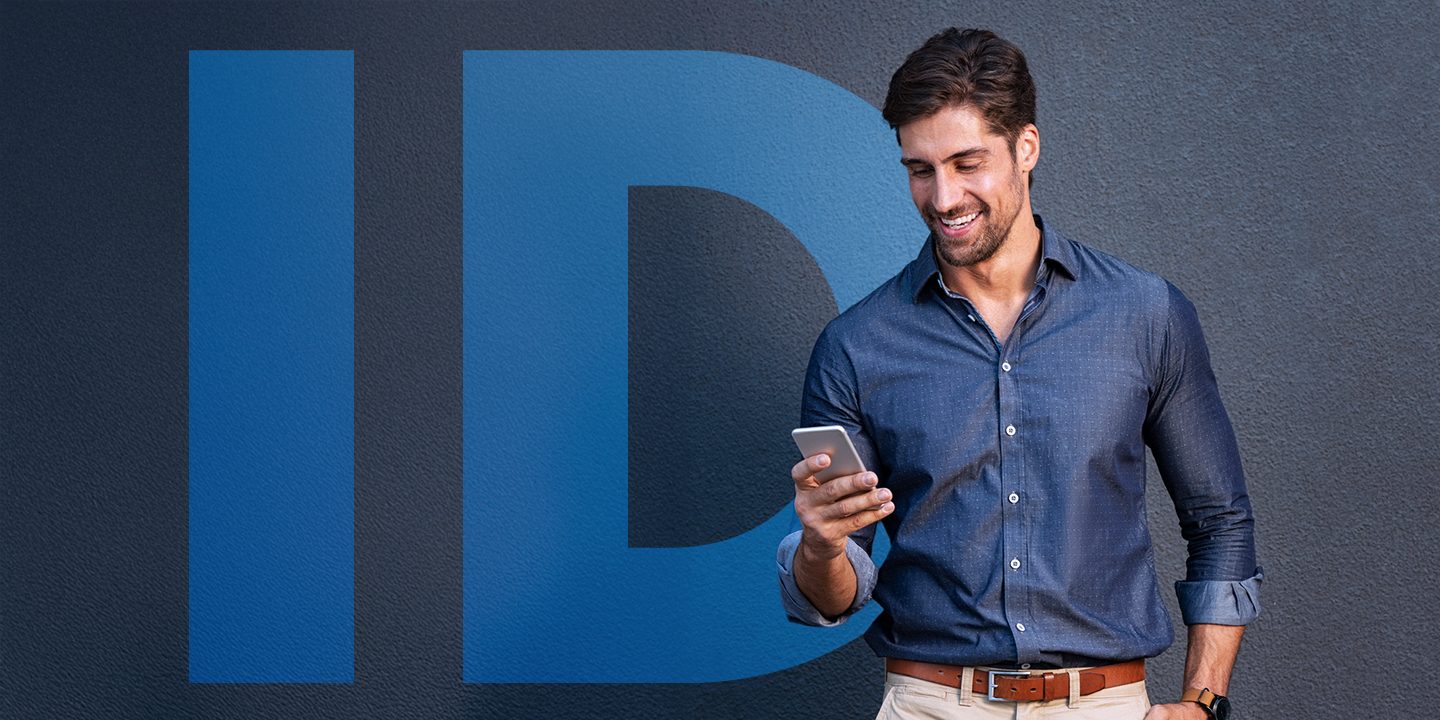 A man looking at a smartphone while standing in front of a wall with the word “ID” displayed.