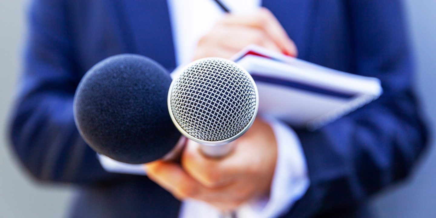 Deux microphones tenus par une personne avec un carnet à la main.