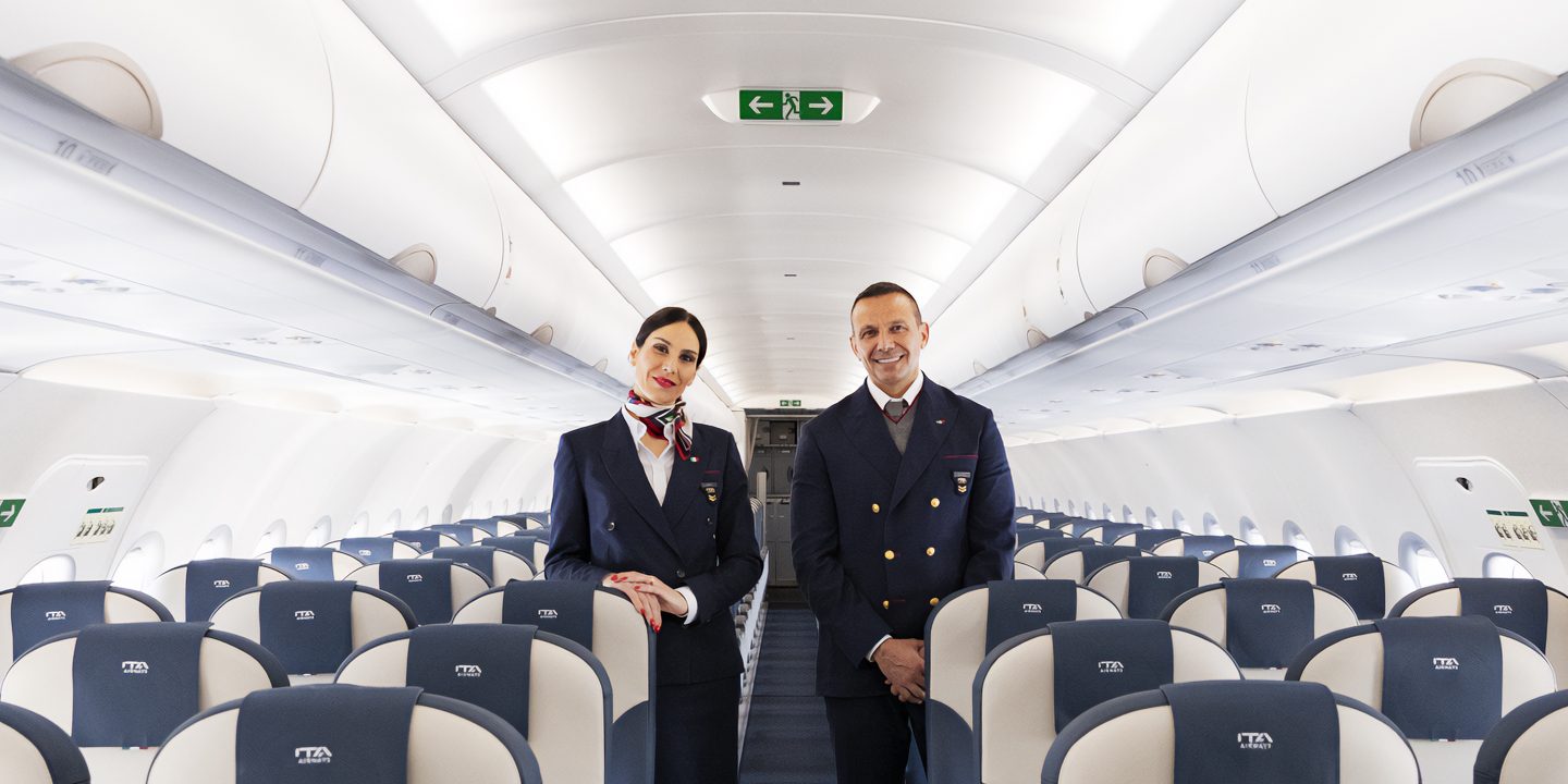 Assistenti di volo in divisa sorridono nel corridoio di un aereo passeggeri.