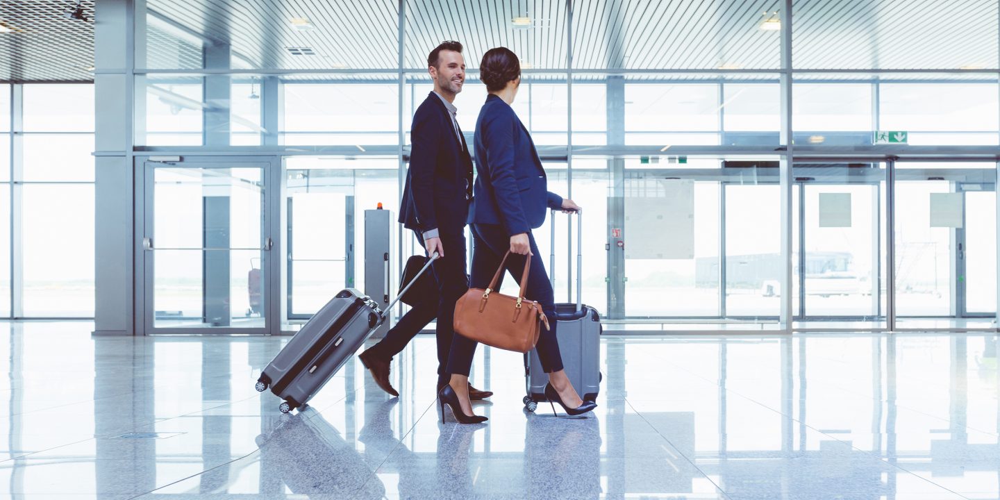 Two adults walking through the airport with suitcases and trolleys.