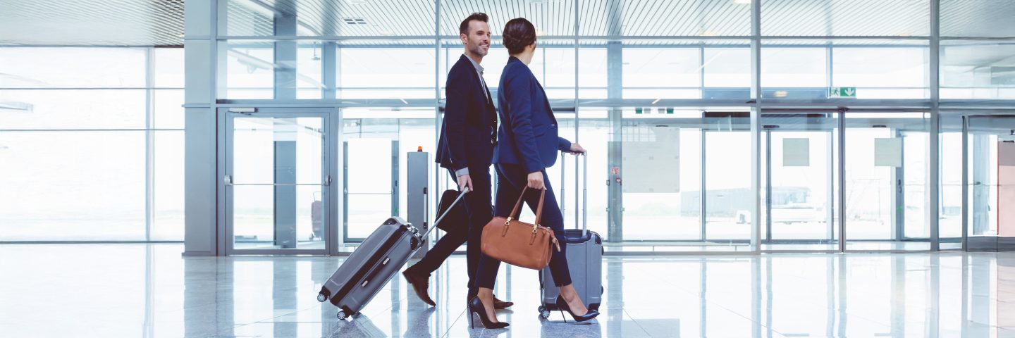 Two adults walking through an airport with bags and suitcases.