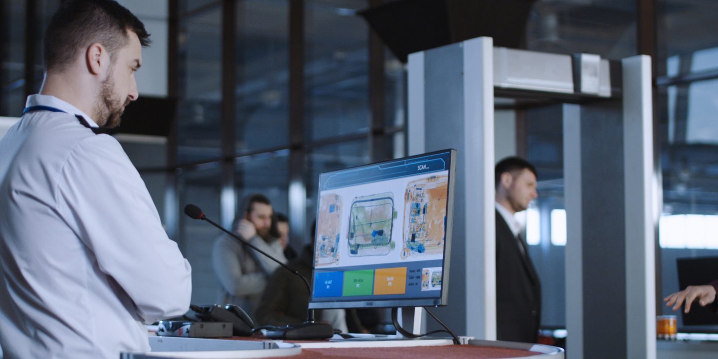 Airport staff member monitoring screens at the security gates.