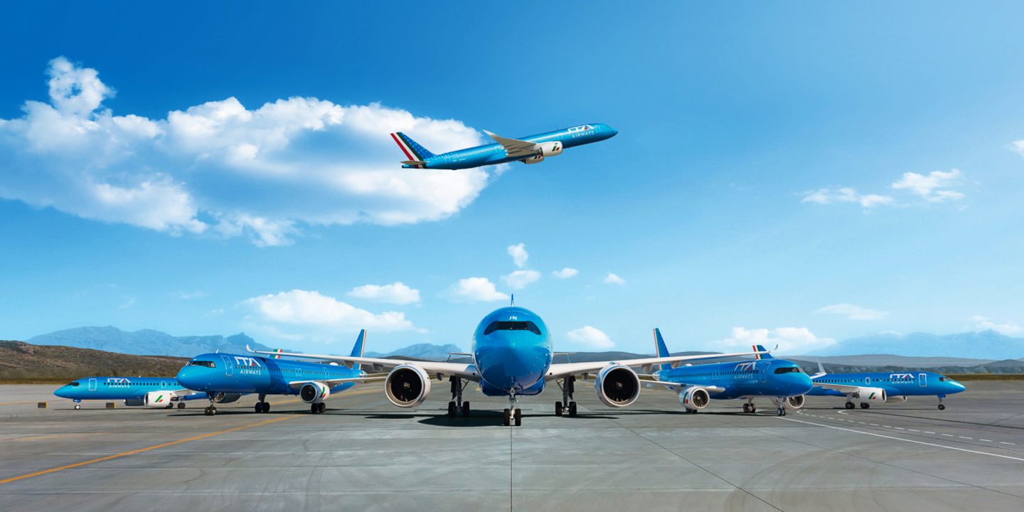 Ένα αεροπλάνο της ITA Airways πετά σε γαλάζιο ουρανό.