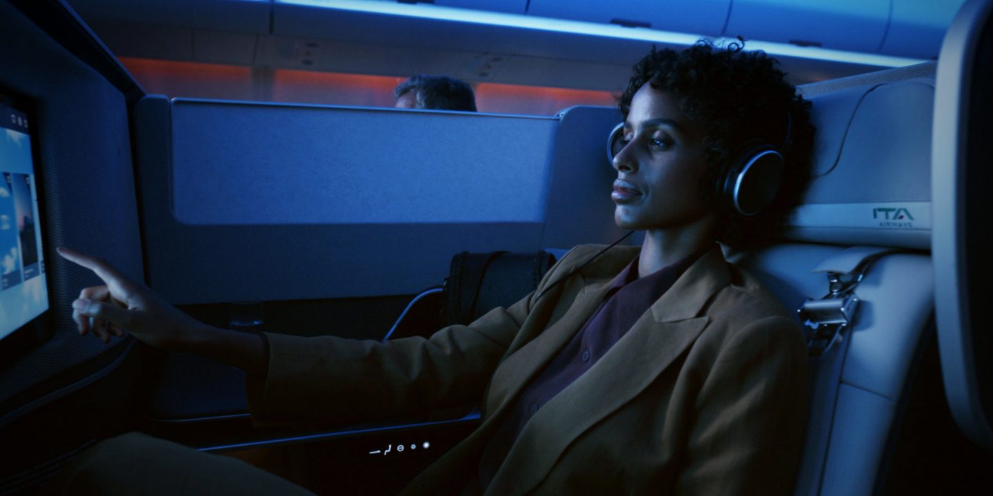 A business class passenger using the in-flight entertainment screen with headphones.
