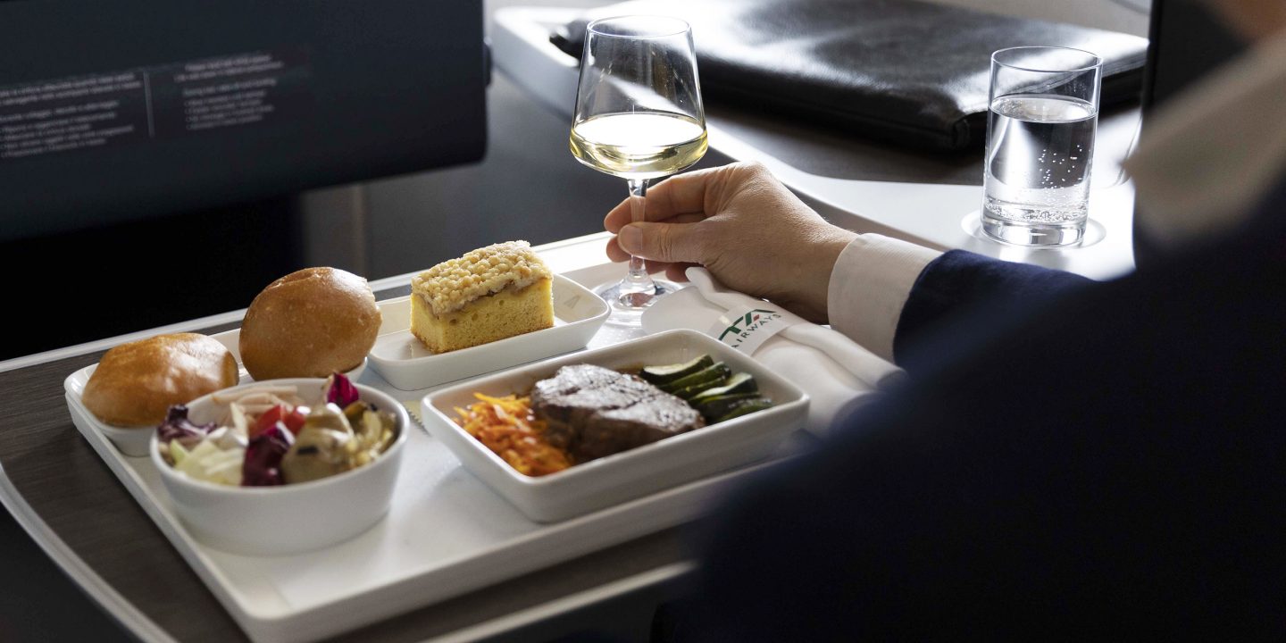 A man sitting on a plane holds a glass of wine.