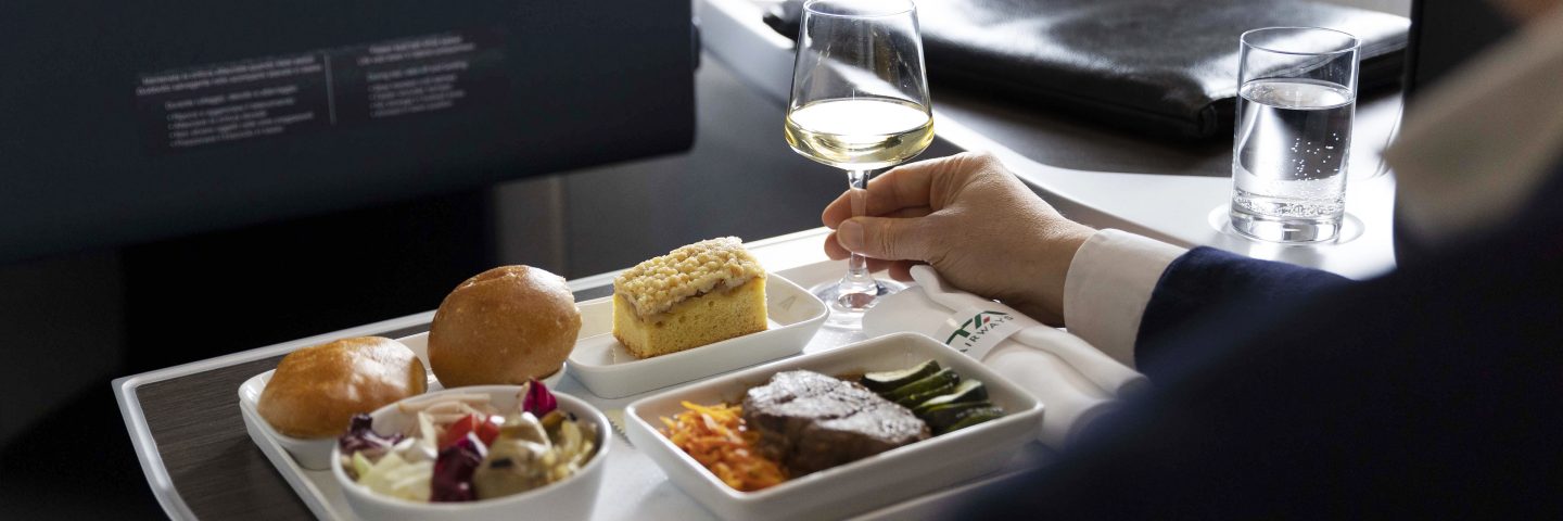 Un homme assis dans un avion, un verre de vin à la main.