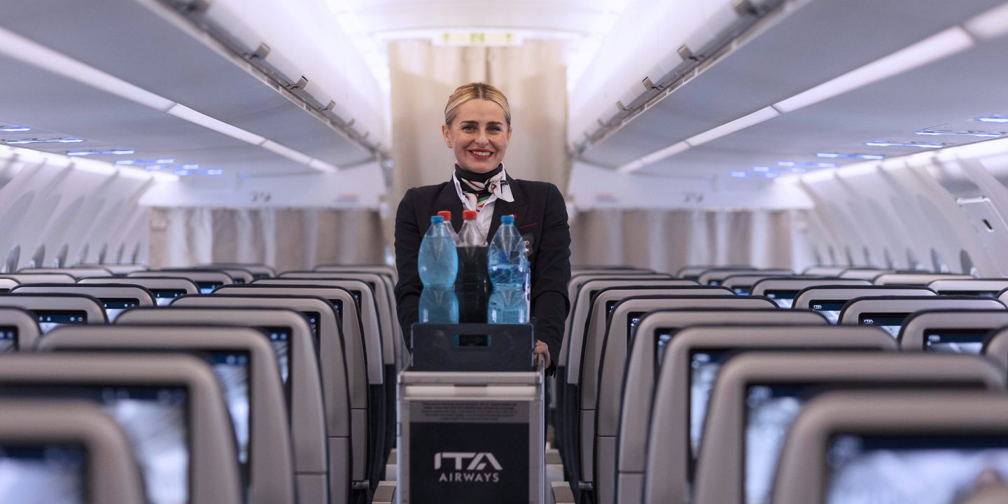 Flight attendant in the aisle of an ITA Airways aircraft with a water cart.
