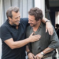 Dois homens rindo juntos com o braço sobre os ombros um do outro.
