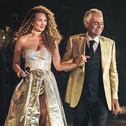 Andrea Bocelli e uma cantora de mãos dadas no palco
