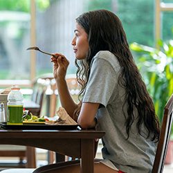 Zendaya com cabelo ondulado longo segurando um garfo enquanto está sentada em uma mesa de jantar.