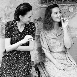 Imagem em preto e branco de duas mulheres conversando e sorrindo ao ar livre.