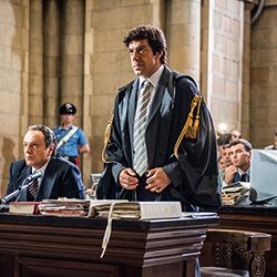 Um homem vestindo uma toga de advogado, em pé em um ambiente de tribunal.