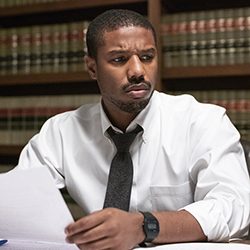 Michael B. Jordan segurando papéis em frente a estantes de livros jurídicos.
