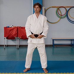 Um homem em pé sobre um tapete azul usando um uniforme branco de artes marciais.