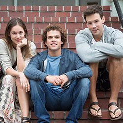 Três jovens amigos sentados juntos em degraus de tijolos ao ar livre.