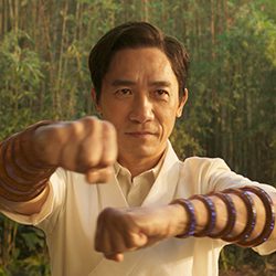 Tony Leung com uma roupa branca empunhando anéis brilhantes nos antebraços.