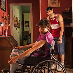 Um jovem em uma cadeira de rodas olhando para trás para outro homem em pé atrás dele.