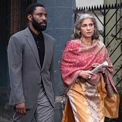 John David Washington e Dimple Kapadia caminham juntos ao ar livre.