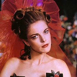 Claudia Gerini como uma noiva com um grande véu vermelho na cabeça.