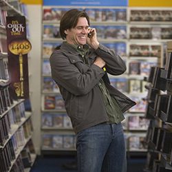 Jim Carrey falando ao celular e rindo em uma locadora de vídeo.