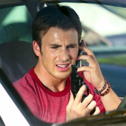 Homem dentro de um carro falando ao telefone enquanto segura uma arma.