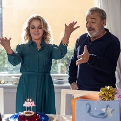 Um homem e uma mulher comemoram um aniversário em frente a um bolo com velas.
