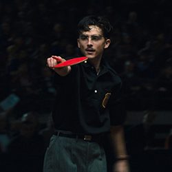 Timothée Chalamet de bigode segura uma raquete de pingue-pongue vermelha.